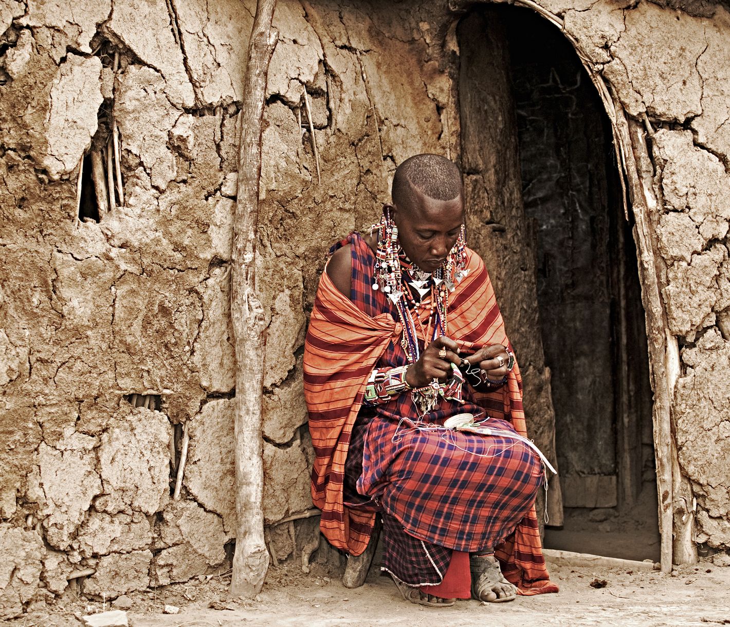 Eine Masai-Frau knüpft Perlenschmuck vor einer traditionellen Hütte.