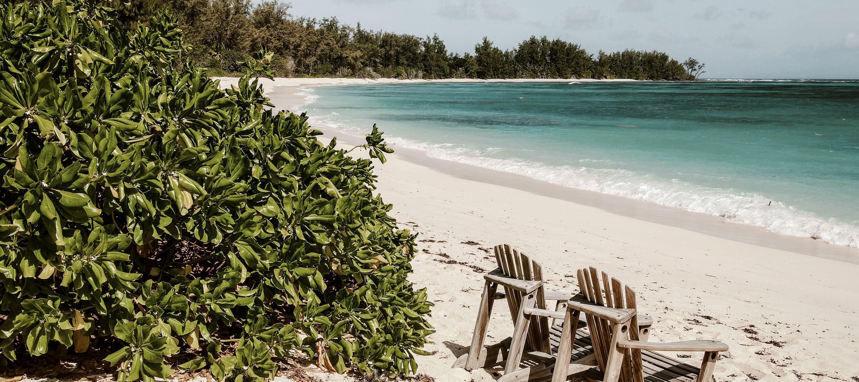 Zwei Stühle am langen Sandstrand von Denis Island mit Blick auf das türkisfarbene Wasser der Lagune