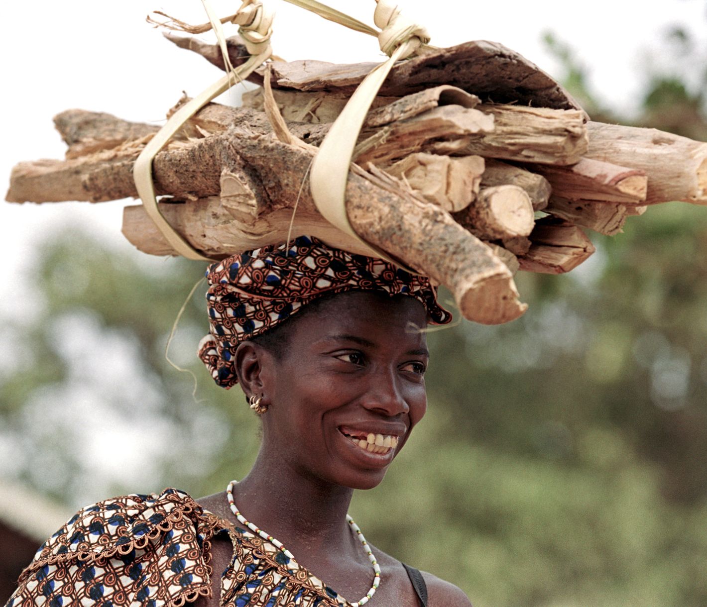 Eine Gambierin spaziert mit einem Holzbündel auf dem Kopf.