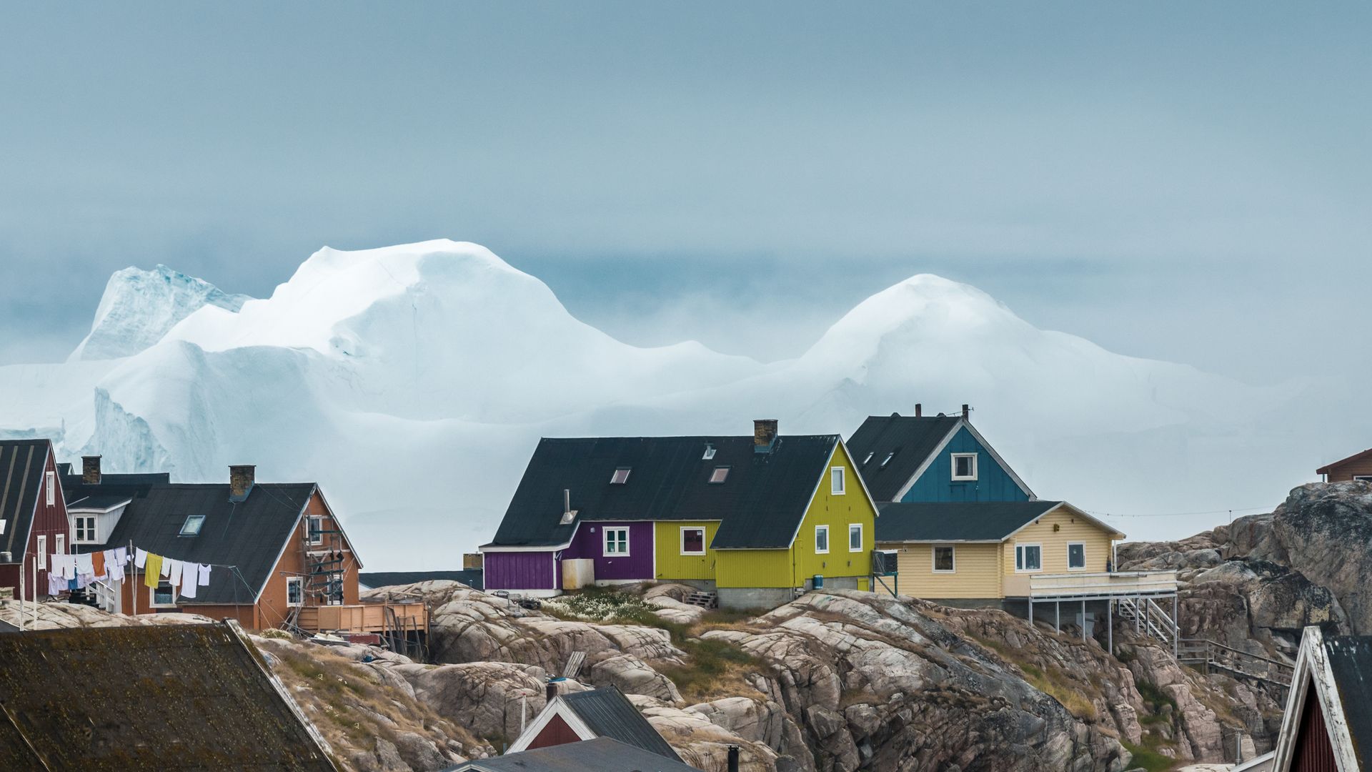 Farbige Häuser thronen vor der Kulisse von gestrandeten Eisbergen in Ilulissat.