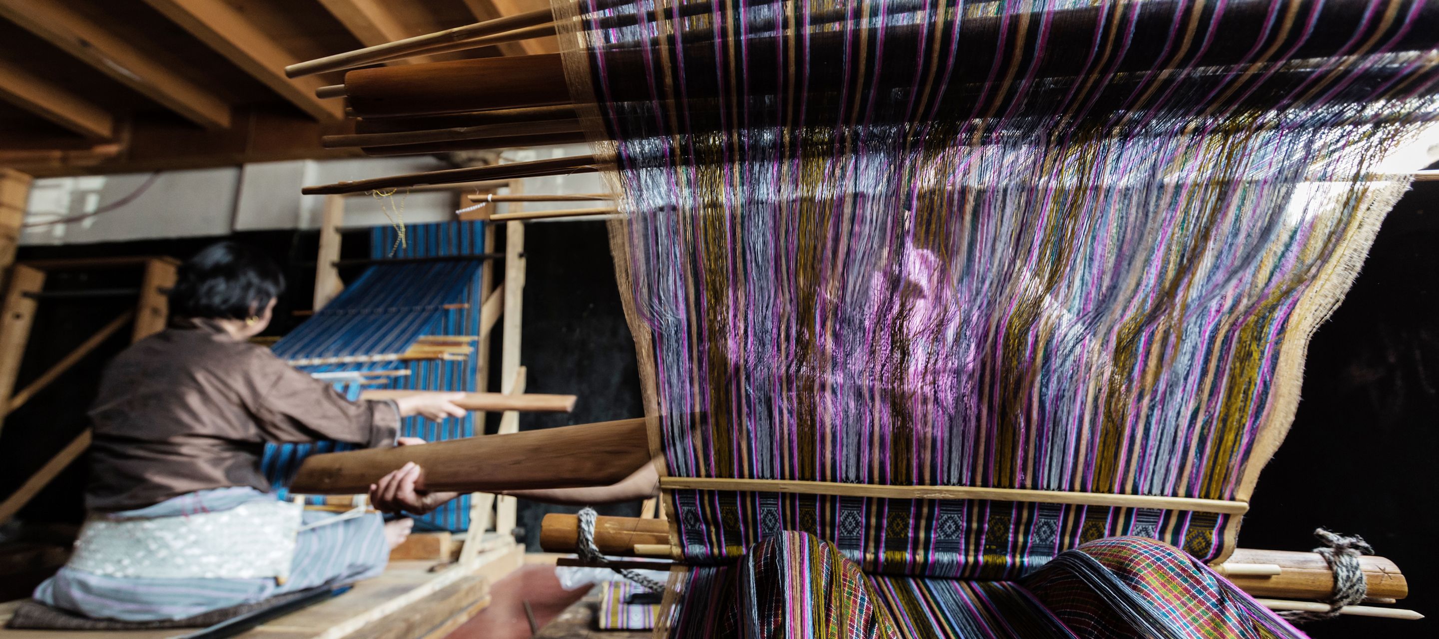Weberinnen und Weber arbeiten auf traditionellen Webstühlen