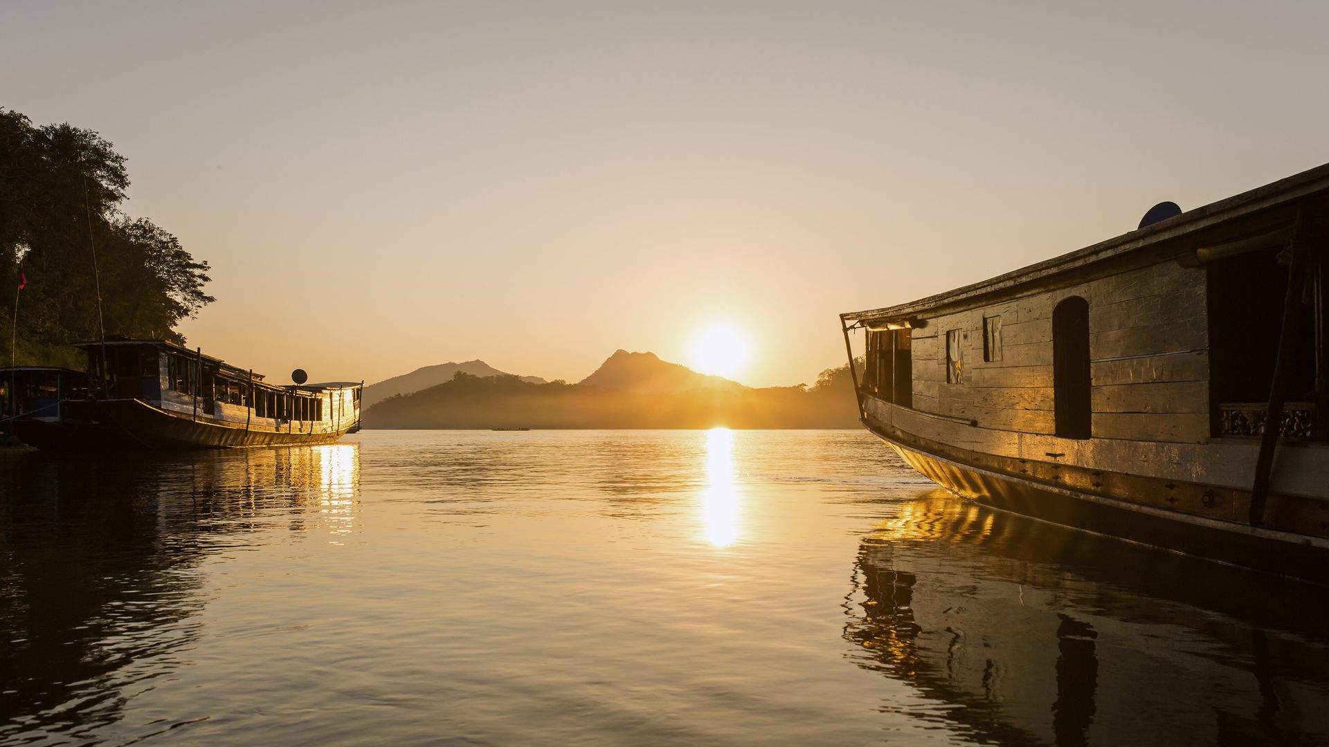 Les bateaux traditionnels laotiens se reflètent sur le Mékong au coucher du soleil.