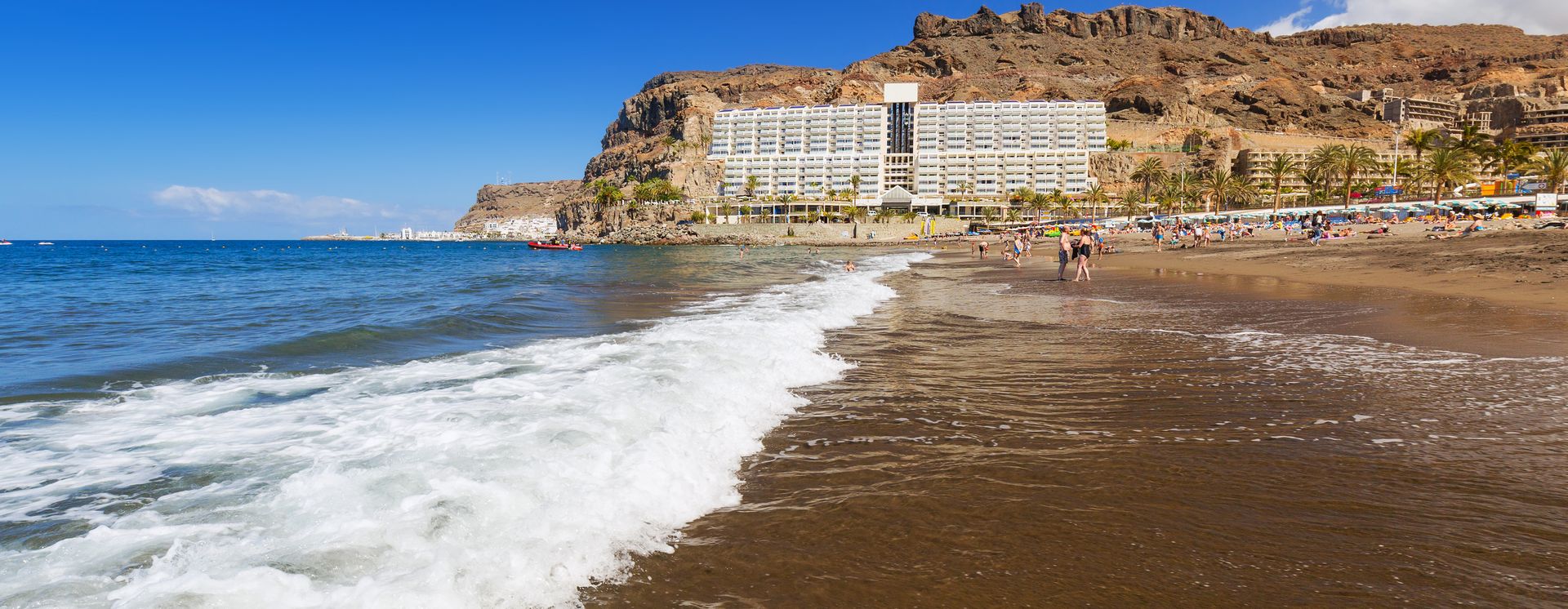 Blick auf den flach abfallenden, dunklen Sandstrand Playa de Taurito