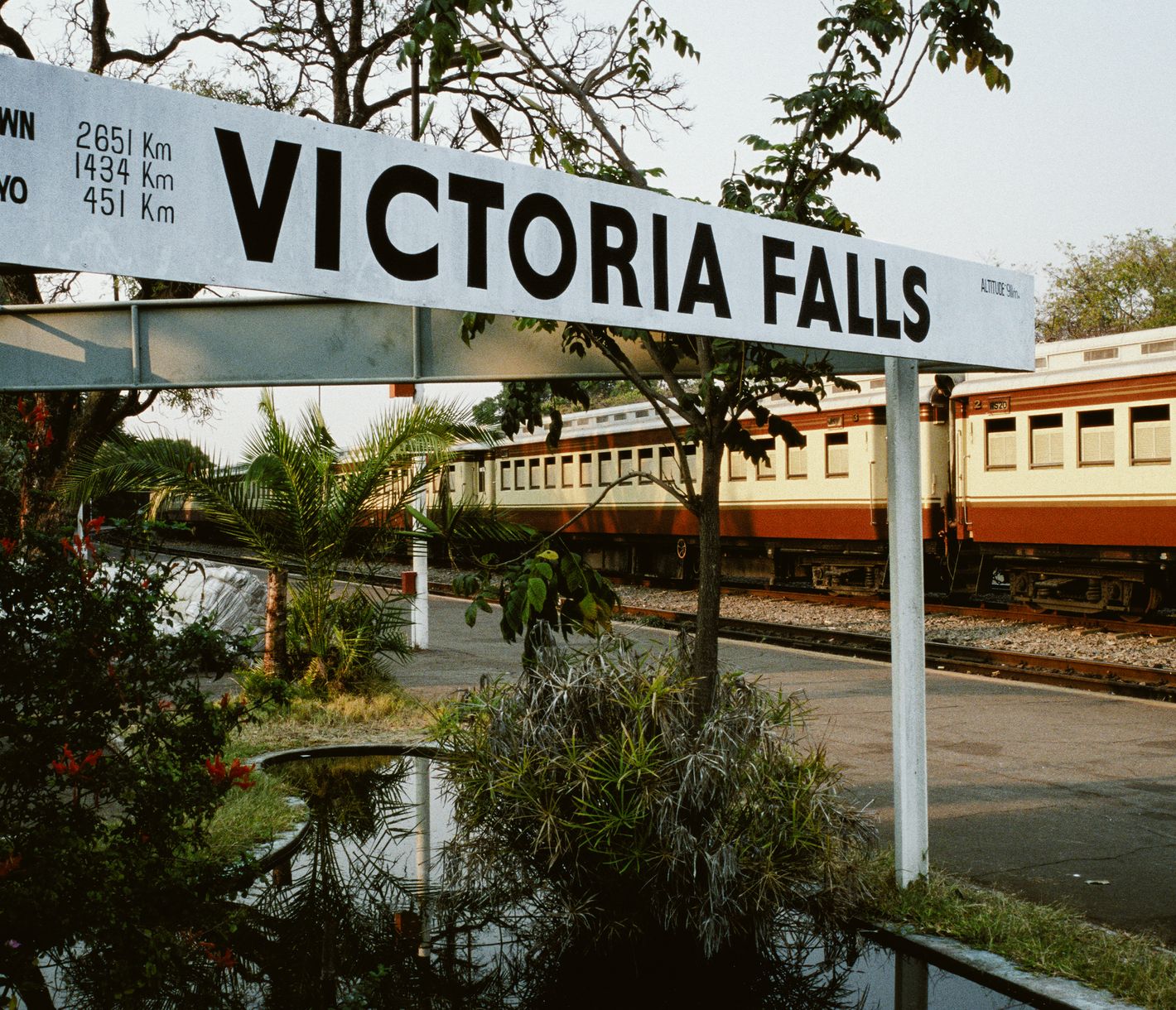 Bahnhofsschild von Victoria Falls mit einem Vintage-Zug im Hintergrund