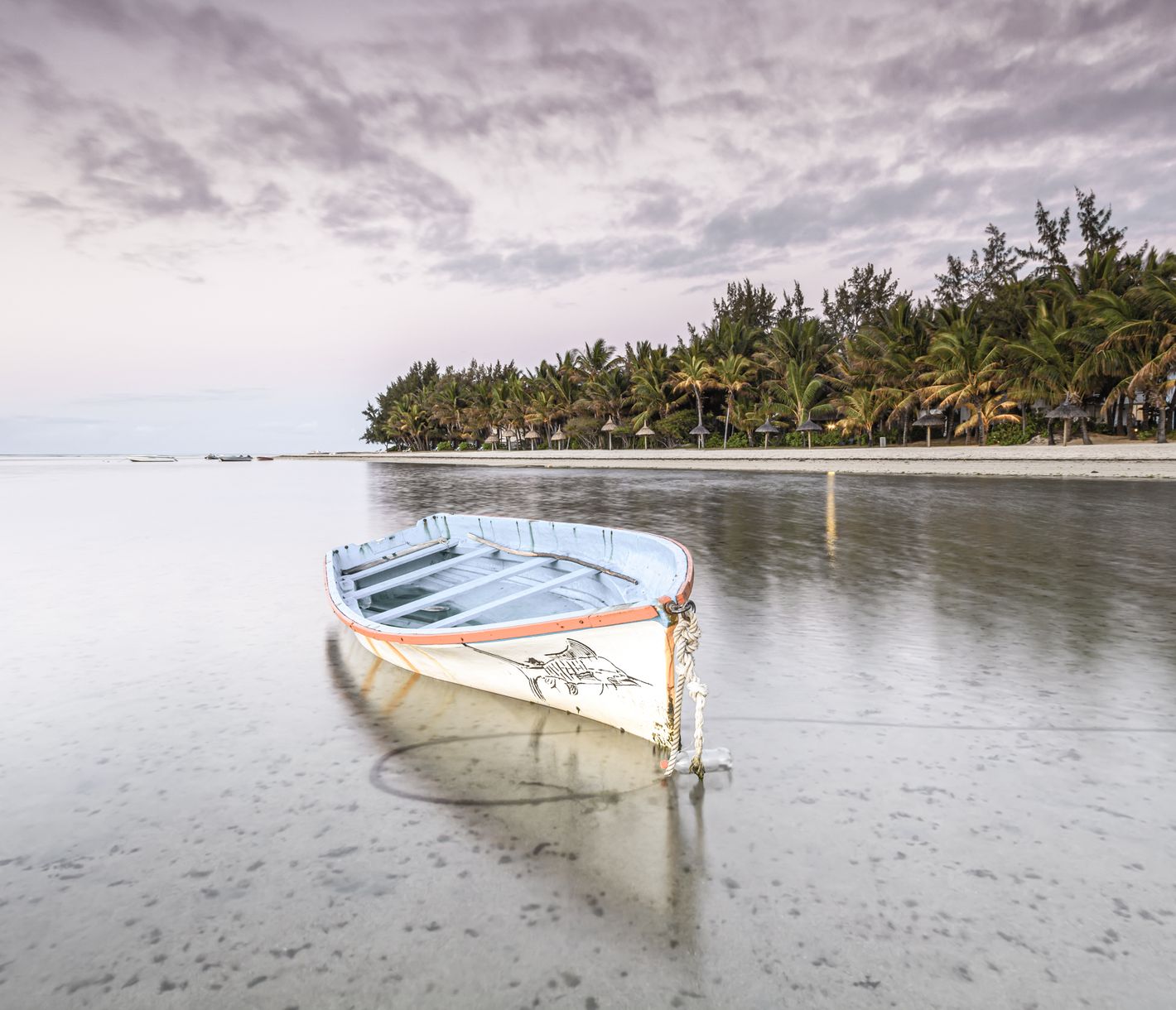 Ruhendes Fischerboot am langen Strand vor Blue Bay im Licht des Sonnenuntergangs